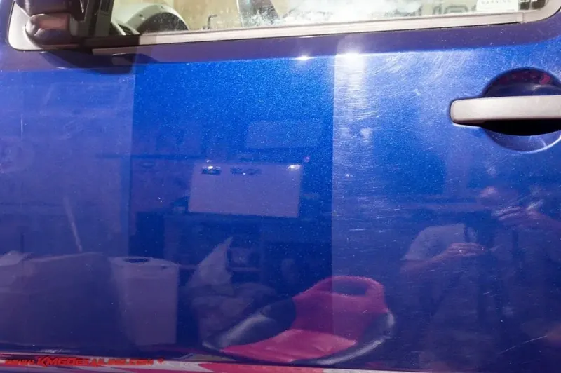 Blue car door during paint correction, showing deep gloss